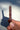 A polished  berry quartz crystal point held between fingers, casting a sharp shadow on a white background.