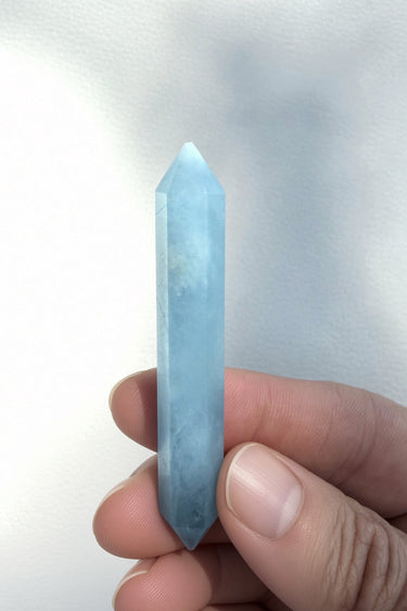 A light blue pointed crystal wand held between fingers against a plain light background.
