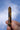 A hand holding a pointed tiger's eye crystal tower against a blue sky with light clouds.